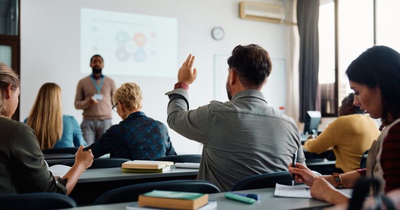 Article: Mastering Change in Higher Education | Man in crowded classroom with hand raised during a lecture